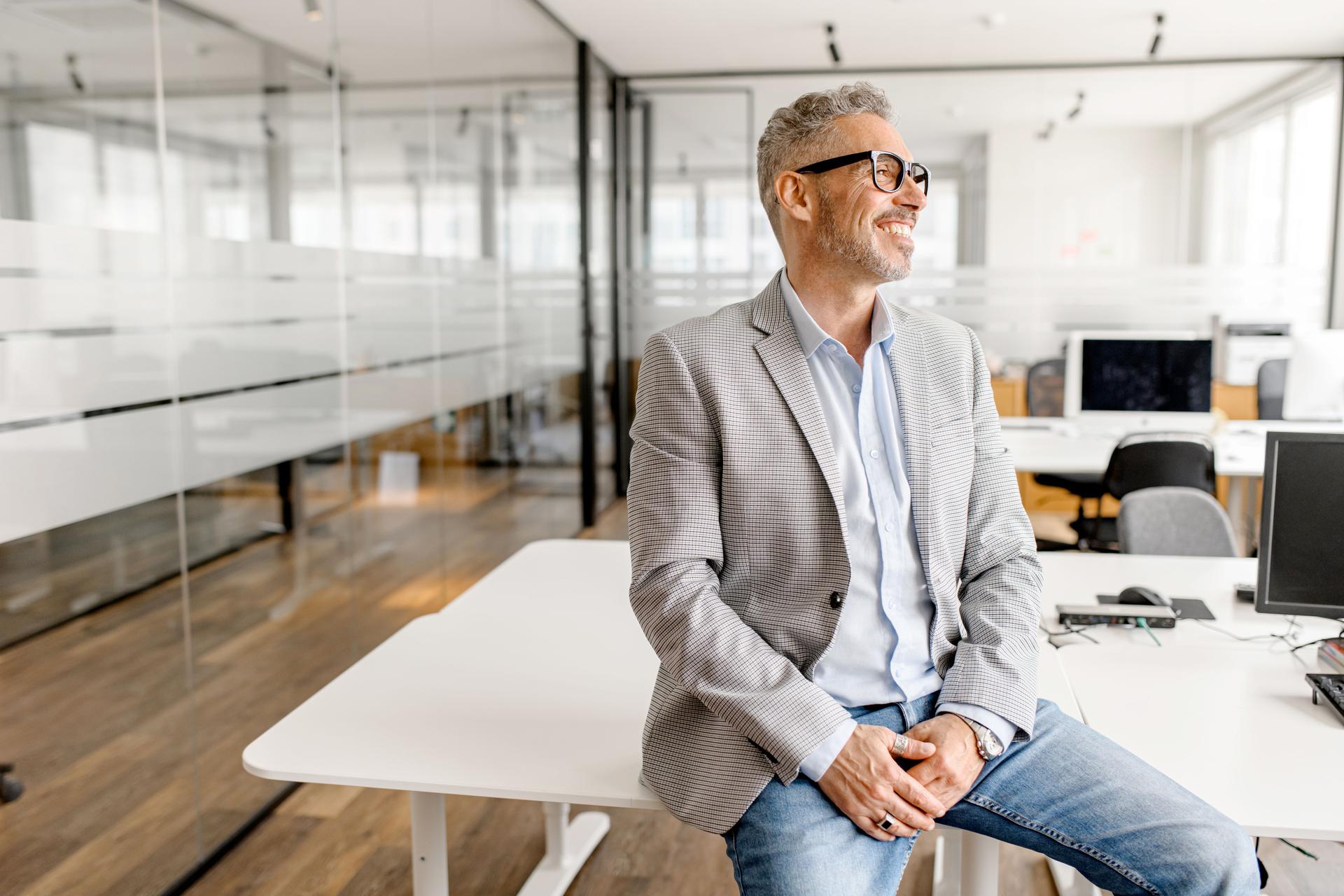 Serene modern middle aged businessman in formal wear leaned on the desk looking away