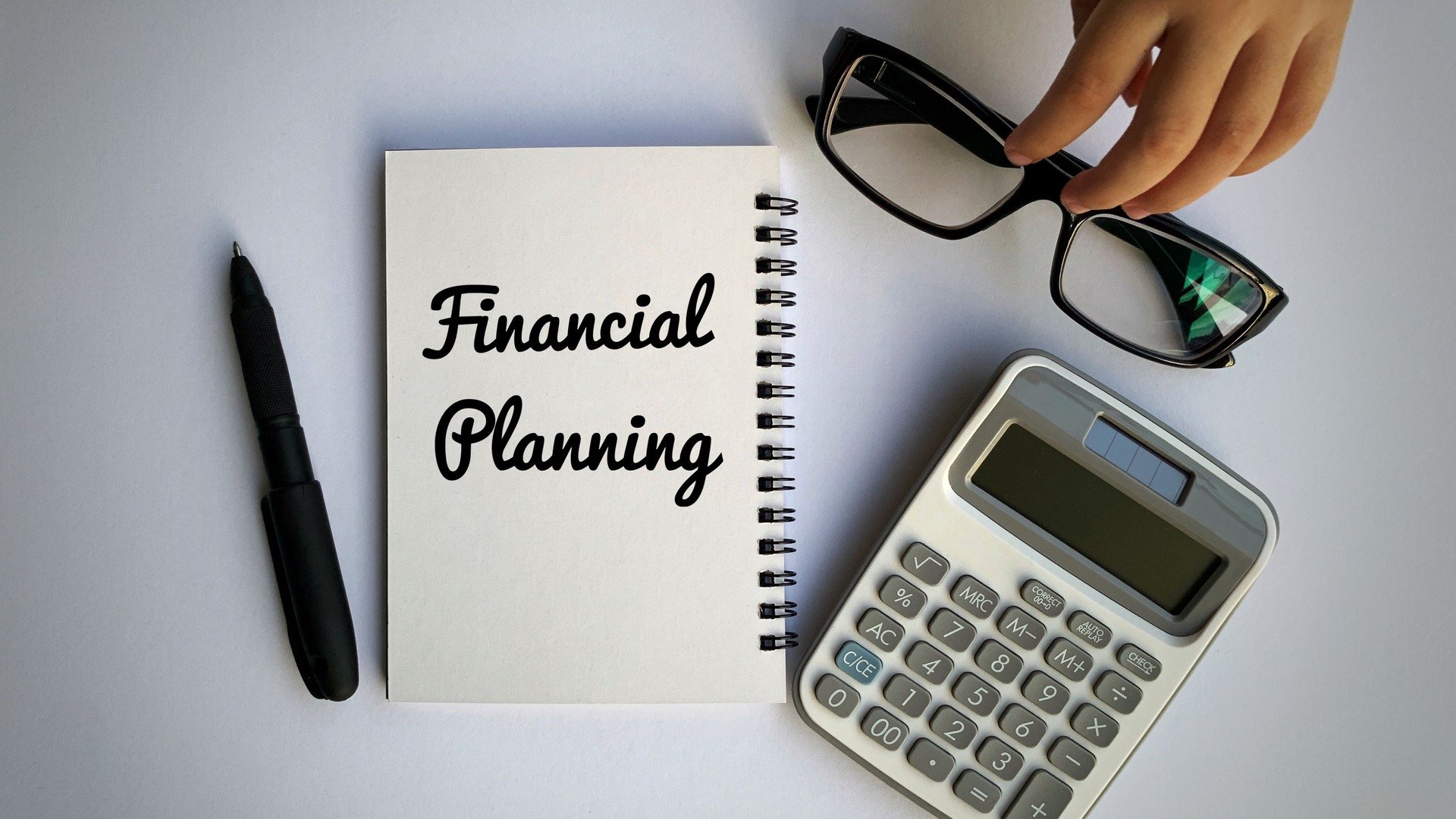 Financial planning text on notepad with hand holding glasses, calculator, and pen background. Business concept.